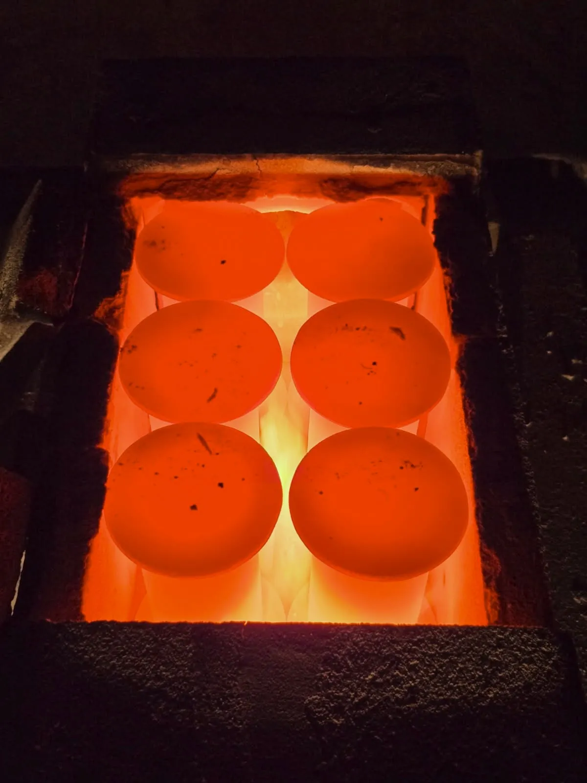 Six crucibles glowing red-orange inside a US Carbon graphitization furnace.